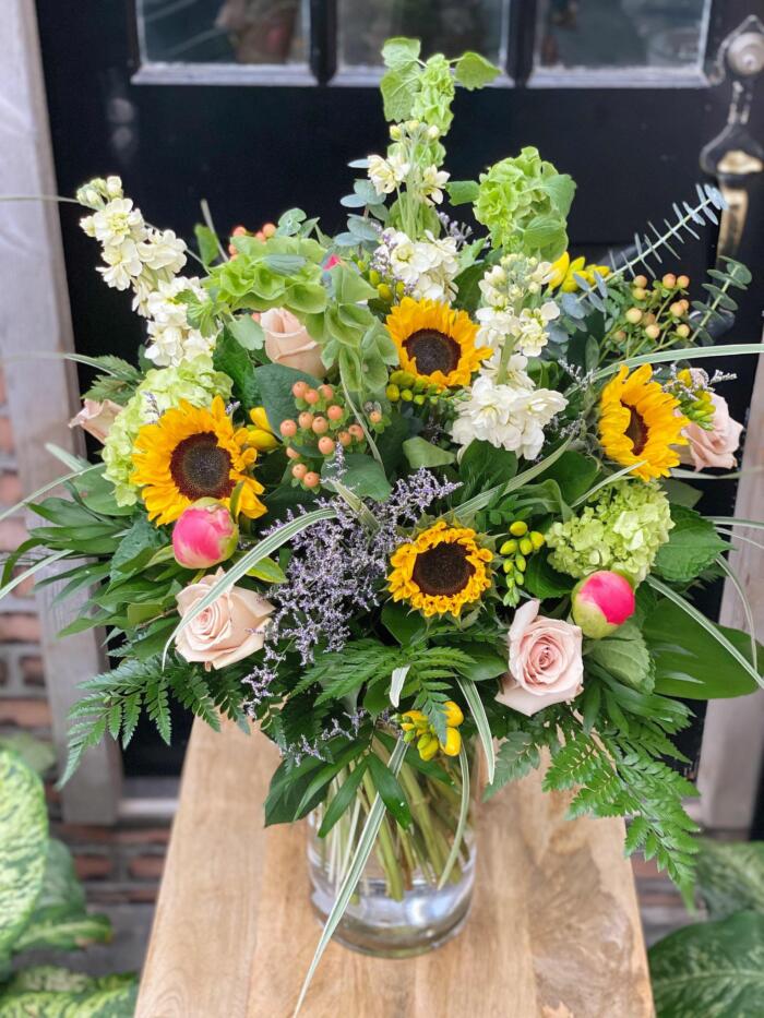 The Watering Can | A Large cheery, garden style bouquet with sunflowers in a large glass vase.