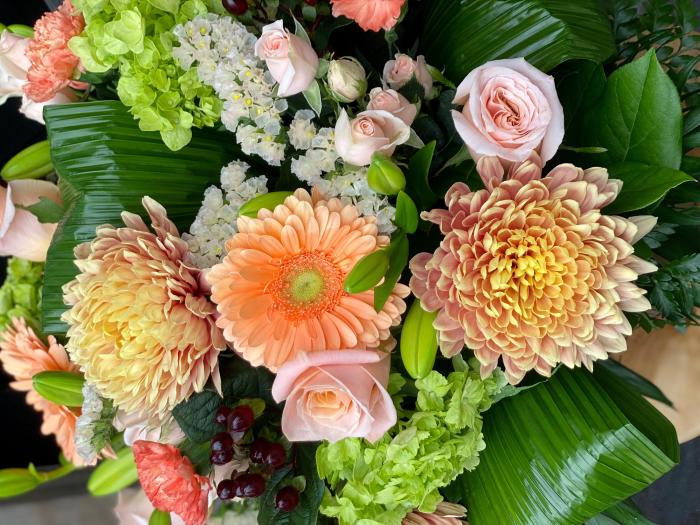 The Watering Can | A close up image of the oragne mums, oragne gerbera daisies, pink roses and green hydrangea in a large bouquet.