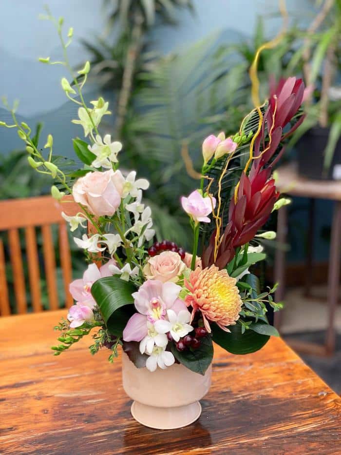 The Watering Can | A tall European style floral arrangement of burgundy, peaches and pink blooms set in a blush container.