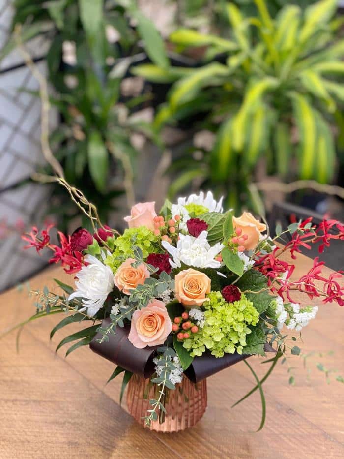 The Watering Can | A large burgundy, blush, green, and white bouquet in a coloured glass vase.