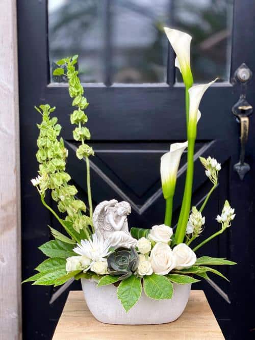 The Watering Can | A large European style arrangment in whites and green with a resting angel statue in an oblong white ceramic container.