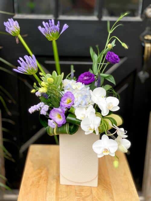 The Watering Can | A modern cascading purple and white bouquet in a rectangular white vase.