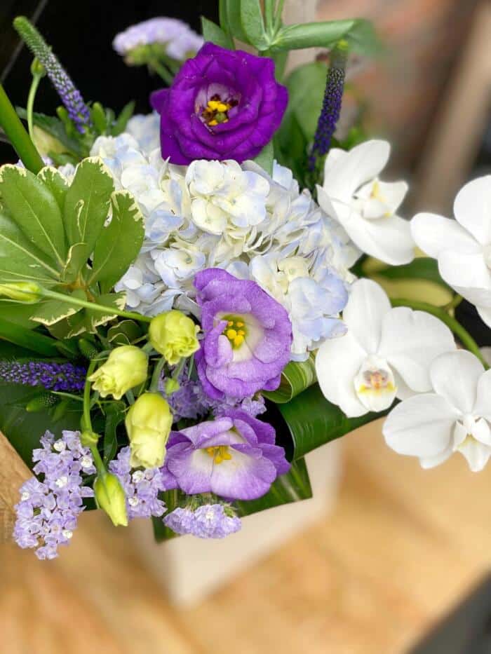 The Watering Can | Image of thelavender hydrangea, purple lisianthus, and white orchids in a large bouquet in vase.