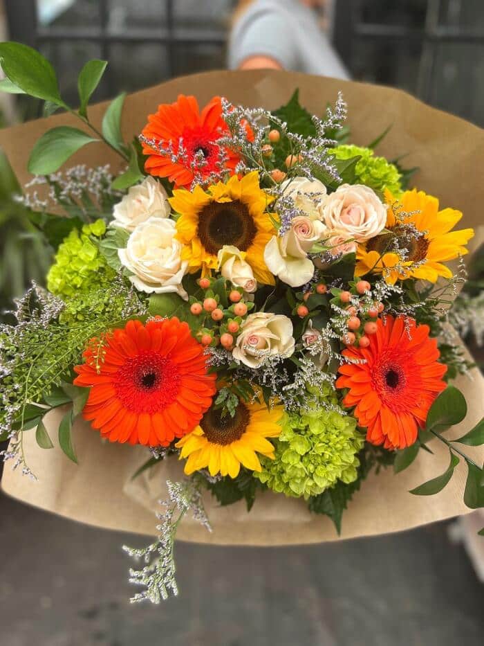 The Watering Can | A summery hand-tied bouquet with sunflowers, orange gerbera daisies and green hydrangea.