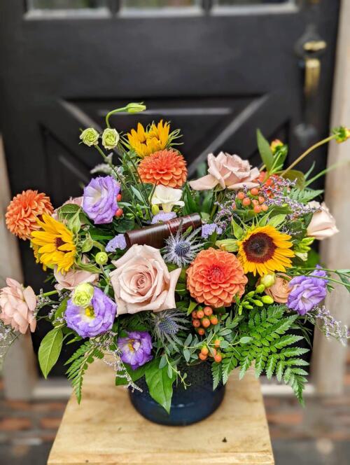The Watering Can | A large orange, yellow, and purple bouquet in a dark blue vase.