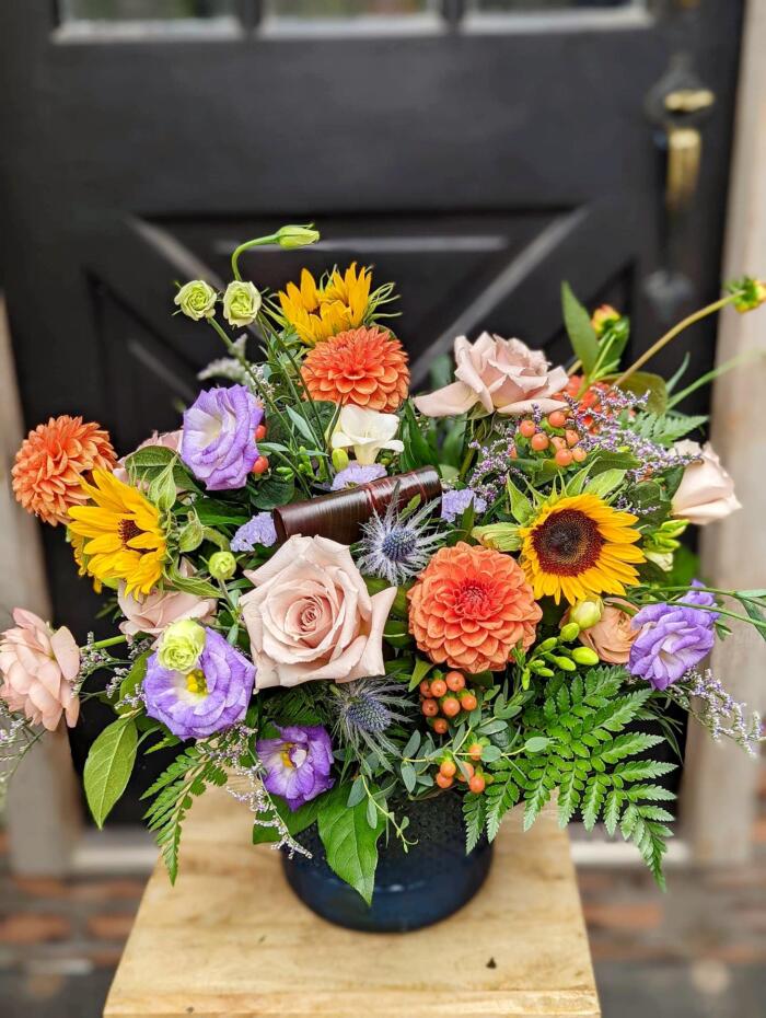 The Watering Can | A large orange, yellow, and purple bouquet in a dark blue vase.