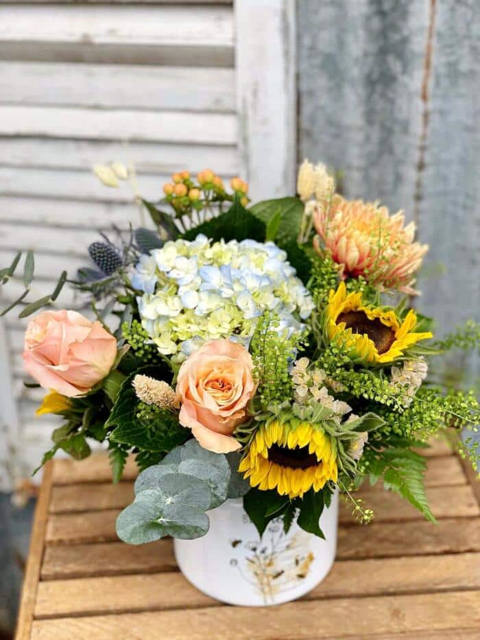 The Watering Can | A beautiful bouquet with sunflowers, roses, and hydrangea in a tin vase.