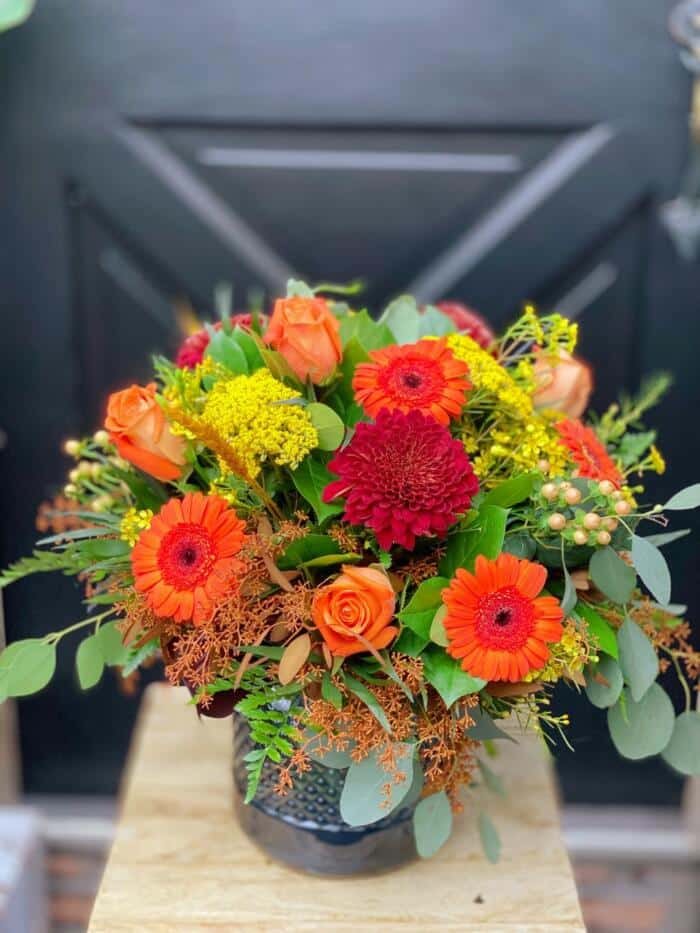 The Watering Can | A large and lush orange, yellow and red bouquet in a blue glass vase.