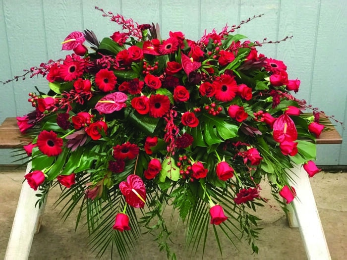 The Watering Can | An all red casket spray made with roses, leucadendron, gerbera daiseies, anthuriums, carnations, annabelle orchids, and hypericum flowers in a lush bed of greens..