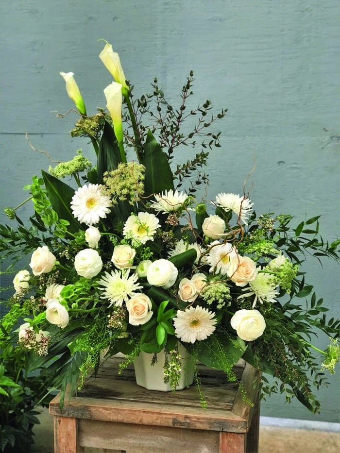 The Watering Can | An asymetrical white side spray with calla lilies, gerberas, roses, mums, rununculus, bells of Ireland, queen Anne's lace, waxflower, curly willow, and a mix of greens.