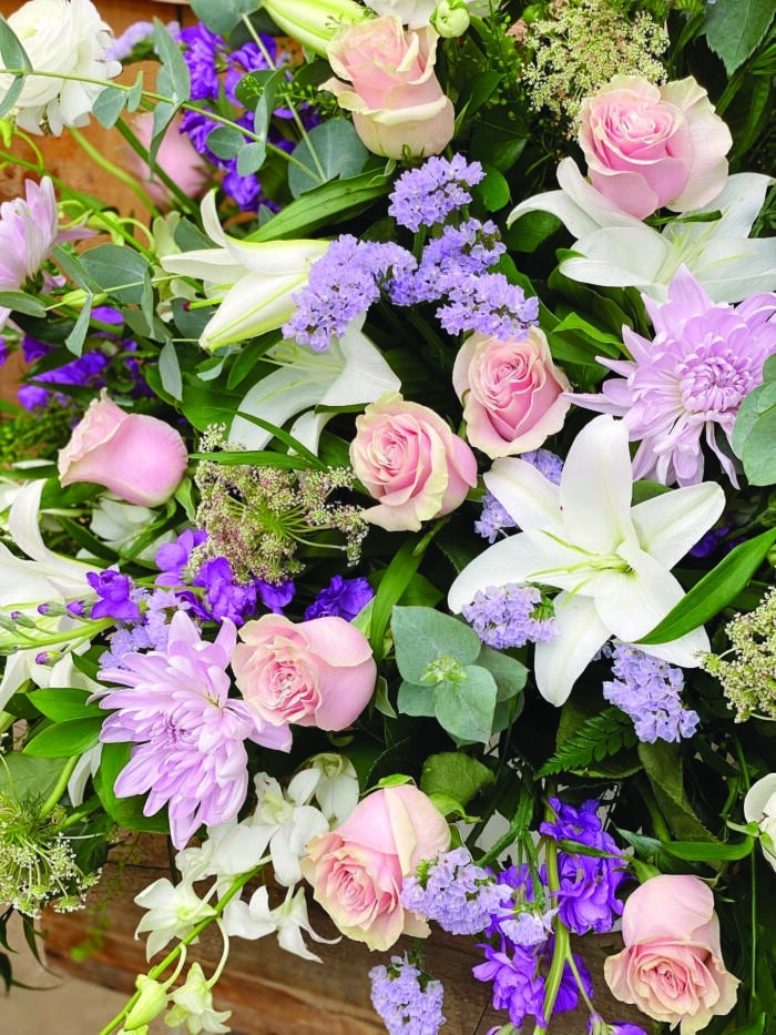The Watering Can | Close up of soft pink roses, white lilies, lavender mums, and blue statice in a side spray.