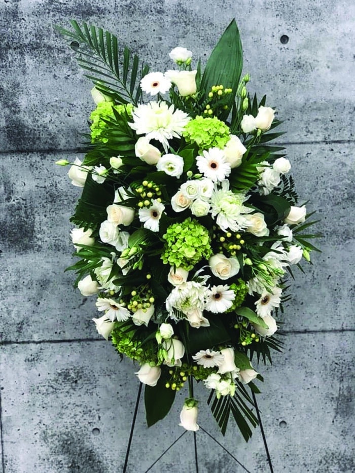 The Watering Can | A very full white easel spray made with roses, lisianthus, hydrangea, mums, hypericum, and gerbera daisies.