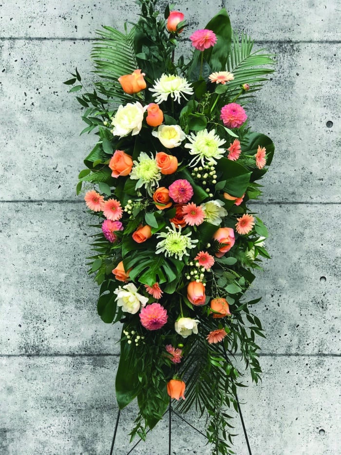 The Watering Can | A coral and white easel spray made with coral roses, white mums, peach/coral dahlias, white peonies, peach gerberas, and white hypericum.