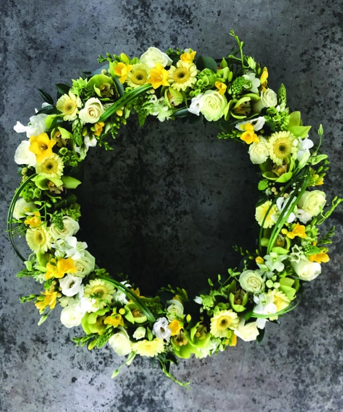 The Watering Can | A large yellow and white wreath with roses, cymbidium orchids, lisianthus, bells of ireland, dendrobium orchids, and freesia.