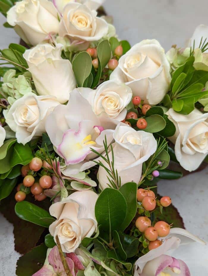 The Watering Can | Close up of white roses, white cymbidium orchids. and peach hypericum in a floral cross.