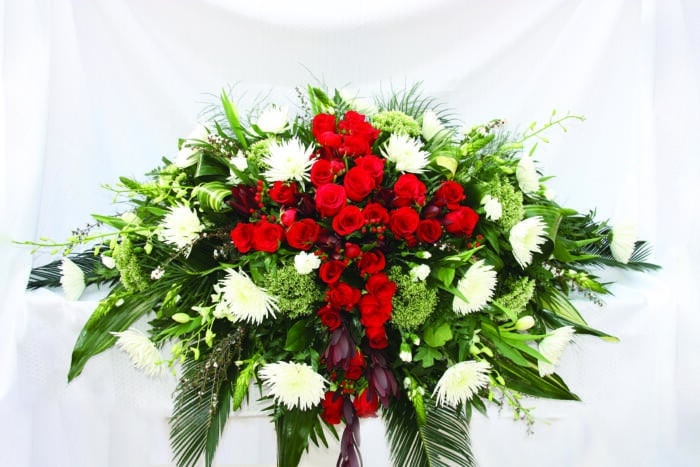 The Watering Can | A rounded green and white casket spray with a cross of red flowers acorss the centre.