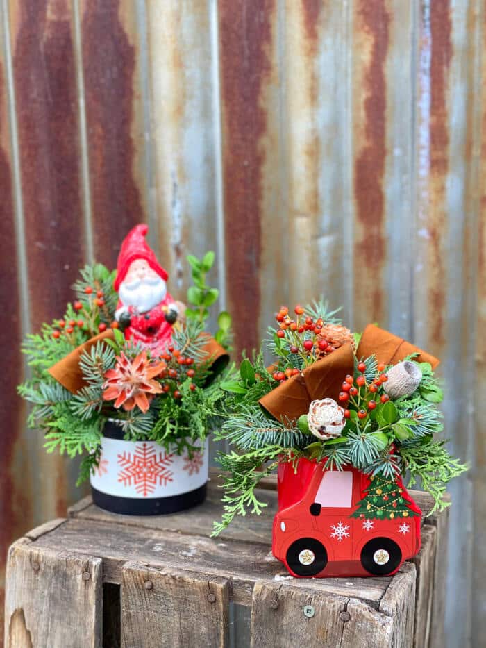 The Watering Can | Two small festive piece, on in a red truck shaped container, the other in a white container with red snowflakes and a santa figuirne plasced in the greens.