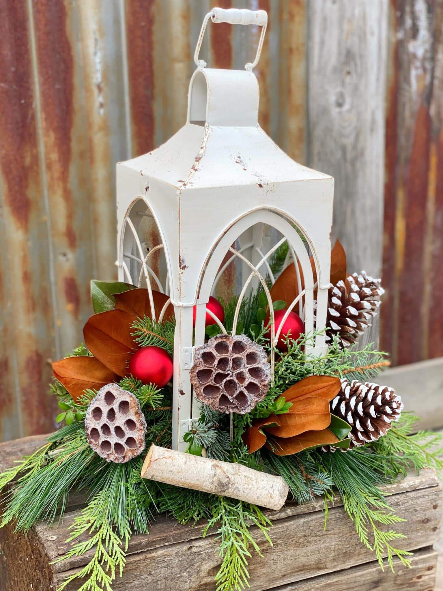 The Watering Can | A large white lantern with an arrangement of winter foliage, natural decorations, and Christmas balls growing out of it.