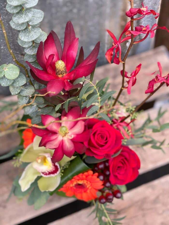 The Watering Can | View from above of the leucadendron, roses, cymbidium orchids, and eucalyptus in a red european style floral arrangement.