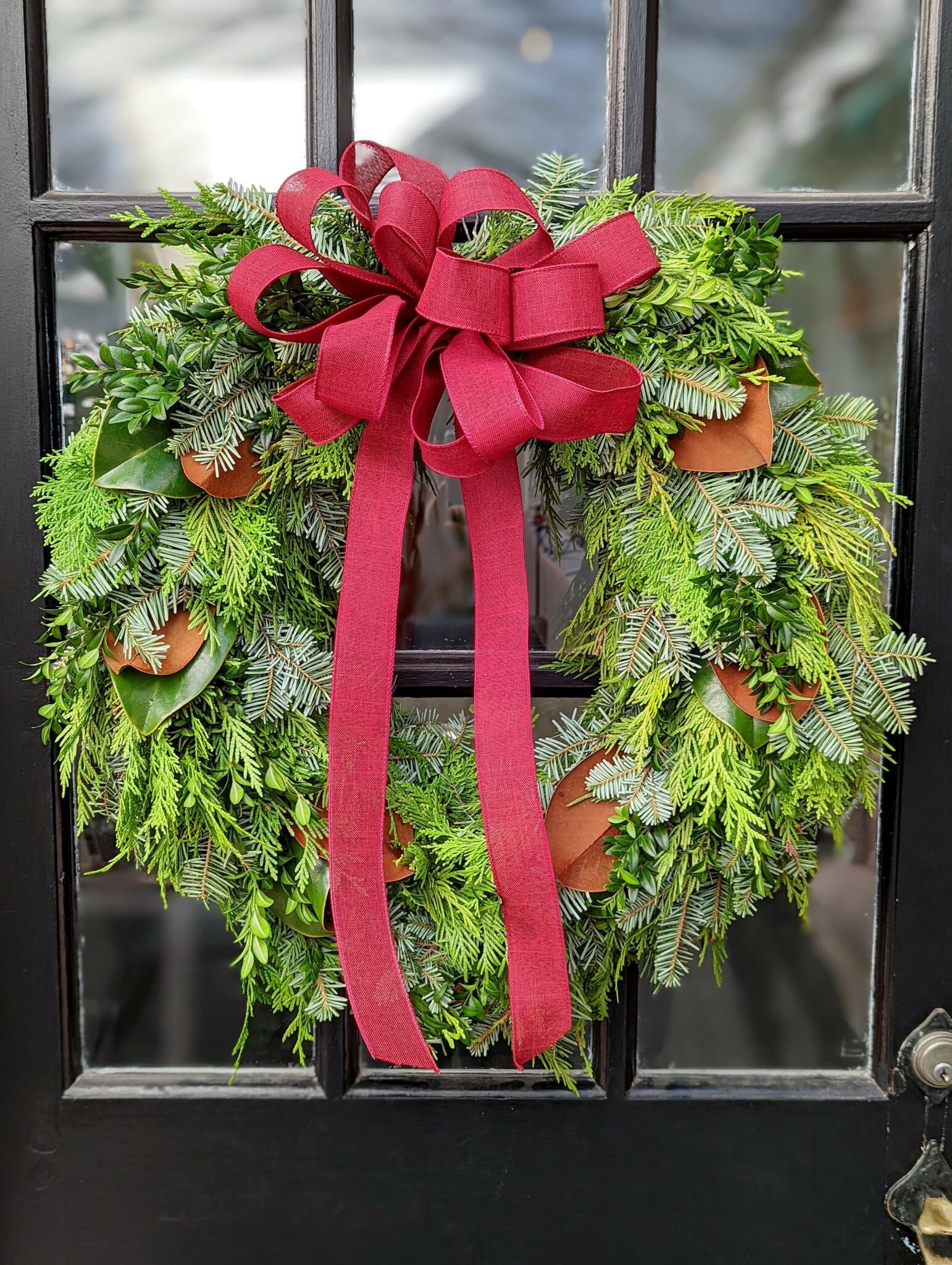 The Watering Can | A wreath made of winter greens and magnolia finished with a large red bow.