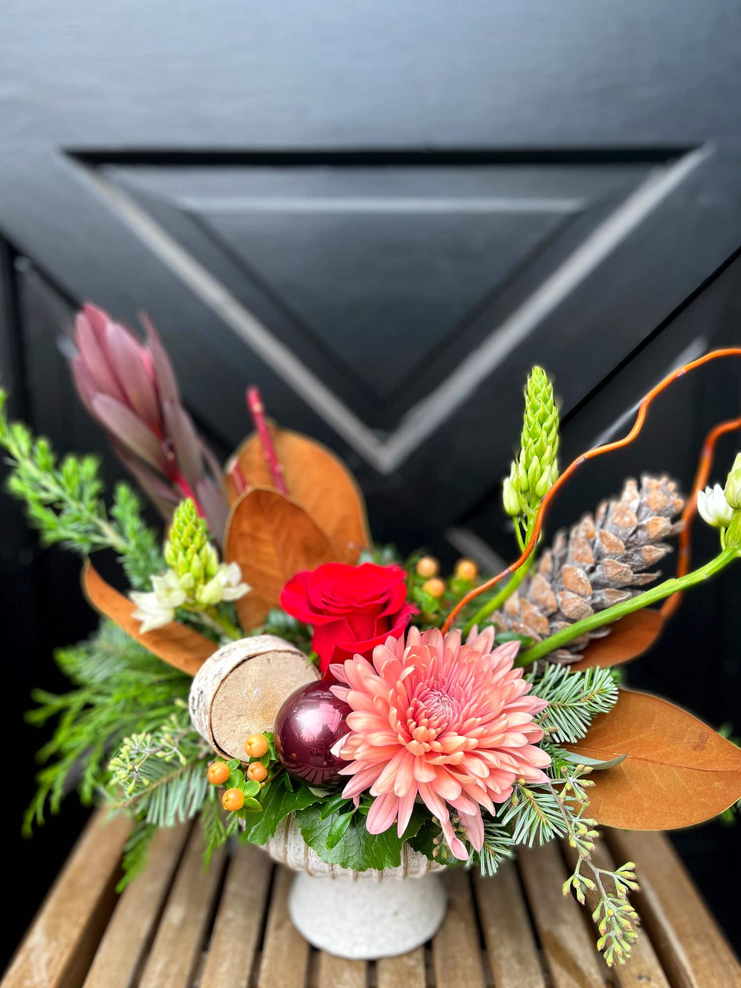 The Watering Can | A red, peach, and burgundy European style arrangement in a white pedestal container.