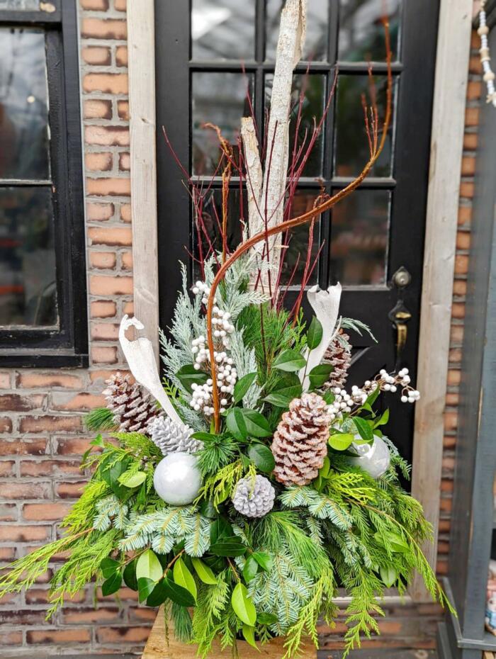 The Watering Can | A large frosted white winter urn full of evergreens, white berries, pine cones, and oranments.